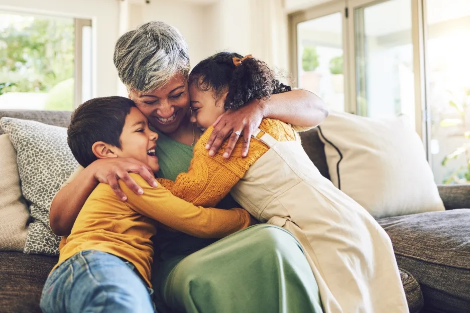 Grandmother and young children sharing a warm hug while sitting together on a sofa in a family home.
